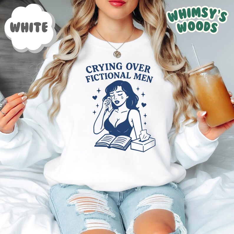K&ouml;nnte beinhalten: Wei&szlig;es Sweatshirt mit dem Text "Crying Over Fictional Men" und einer blauen Illustration einer weinenden Frau. Das Sweatshirt hat auch den Text "Whimsy's Woods" in Gr&uuml;n.
