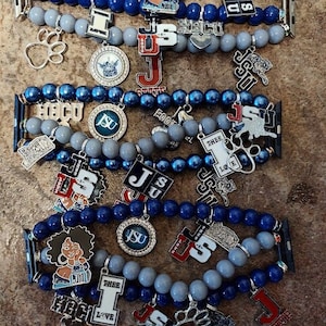 May include: A set of four Apple Watch bands with various charms. The bands are made of gray and blue beads. The charms include a paw print, a crown, a football, a tiger, a letter 'I', and a letter 'J'.