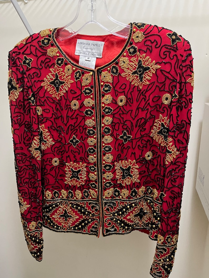 May include: A red beaded jacket with gold and black embroidery. The label reads "Adrianna Papell Evening" and "A. Papell Inc. 1994".