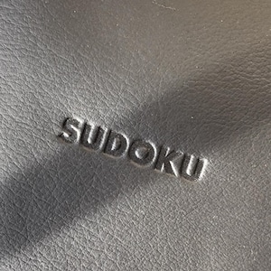 May include: A black leather case with the word "SUDOKU" embossed in the center.
