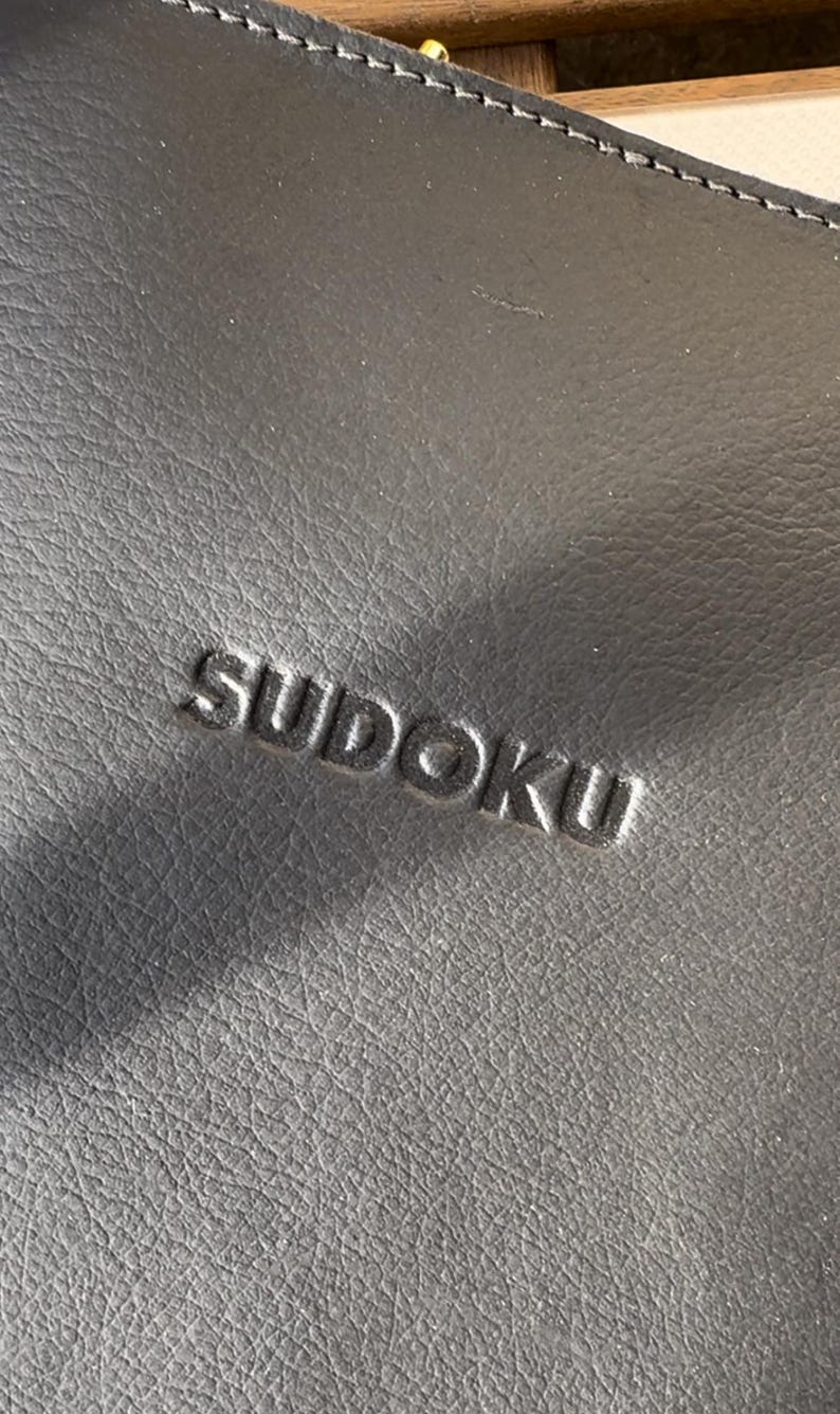 May include: A black leather case with the word "SUDOKU" embossed in the center.