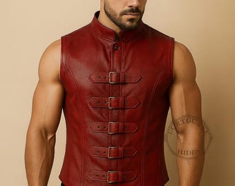 May include: A burgundy leather vest with a mandarin collar and five buckle closures. The vest is sleeveless and has a tailored fit. The image shows a close-up of the vest, highlighting its details and texture.