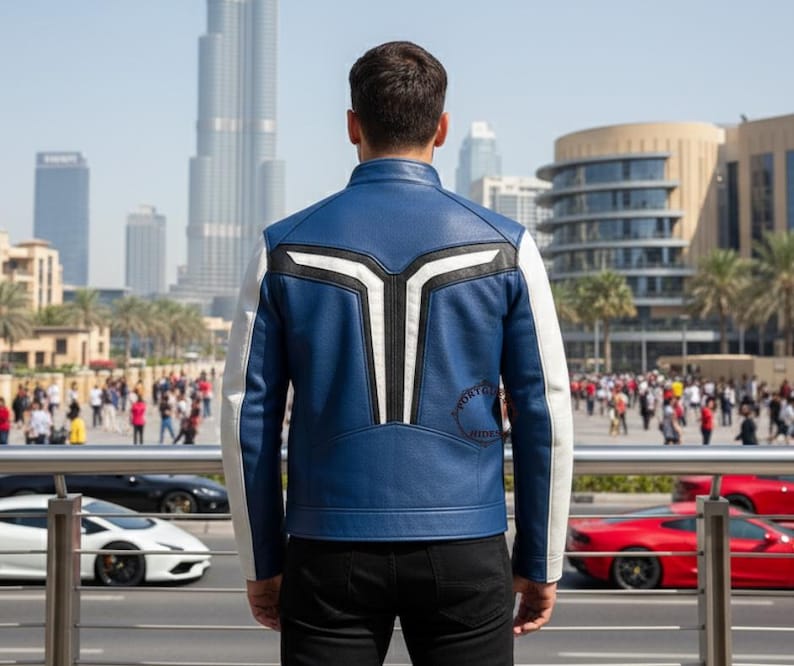 K&ouml;nnte beinhalten: Eine blau-wei&szlig;e Lederjacke mit einem einzigartigen Design auf dem R&uuml;cken. Die Jacke hat einen Stehkragen und wei&szlig;e &Auml;rmel. Die Person steht vor einer Skyline mit moderner Architektur und Palmen.