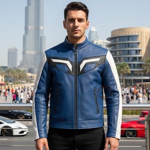 K&ouml;nnte beinhalten: Blaue Lederjacke mit wei&szlig;en und schwarzen Akzenten. Die Jacke hat einen Stehkragen, einen Frontrei&szlig;verschluss und wei&szlig;e &Auml;rmel. Das Design umfasst geometrische Formen auf der Brust. Die Jacke wird &uuml;ber einem schwarzen Hemd getragen.
