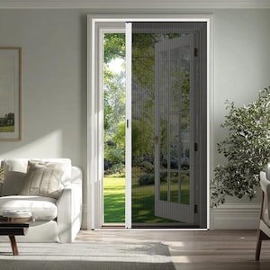 May include: A white framed screen door is partially open, showing a green garden. The screen is dark grey and made of fine mesh. The door is set in a white frame. The interior decor includes a white sofa and a small table.