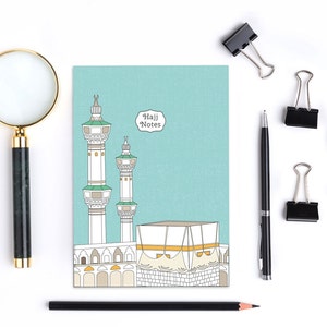 May include: A blue notebook with a drawing of the Kaaba and two minarets. The notebook has the text "Hajj Notes" on the front.