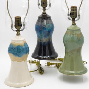 May include: Three ceramic table lamps with brass hardware and shades. The lamps have a bulbous base in cream, blue, and green with a glazed finish. Each lamp is approximately 15 inches tall.