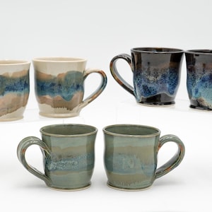 May include: Set of five ceramic mugs with blue, brown, and white glaze. The mugs have a rounded shape and a handle.