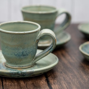 May include: Set of four green and blue ceramic teacups and saucers. The cups have a unique glaze with a mottled effect.