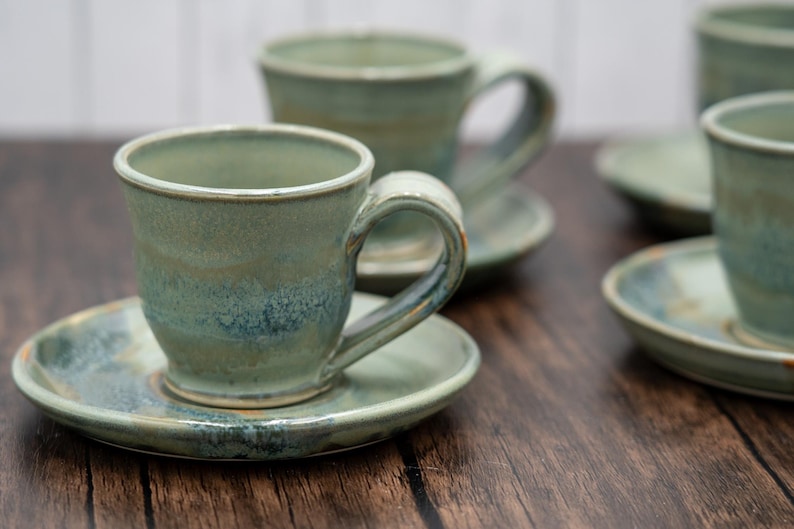 May include: Set of four green and blue ceramic teacups and saucers. The cups have a unique glaze with a mottled effect.