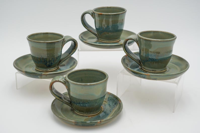 May include: Set of four green and blue ceramic teacups and saucers. The cups and saucers have a mottled glaze with a light green base and darker blue and green streaks.