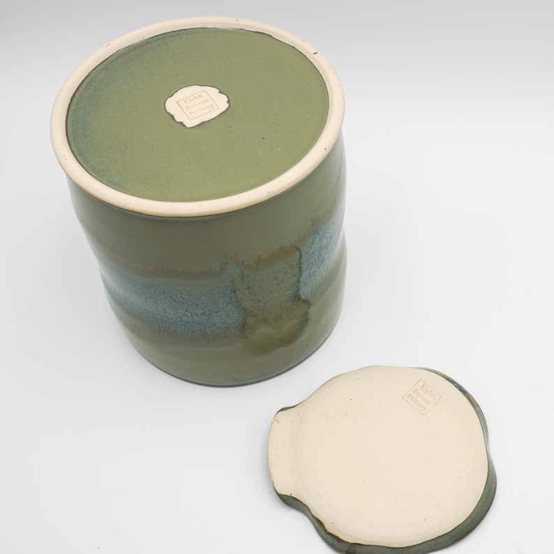 May include: A green ceramic jar with a lid. The jar has a light blue glaze and a darker green glaze. The lid is white with a green rim.