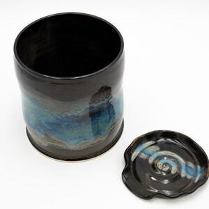 May include: A black ceramic jar with a blue and brown glaze. The jar has a lid with a swirl design.