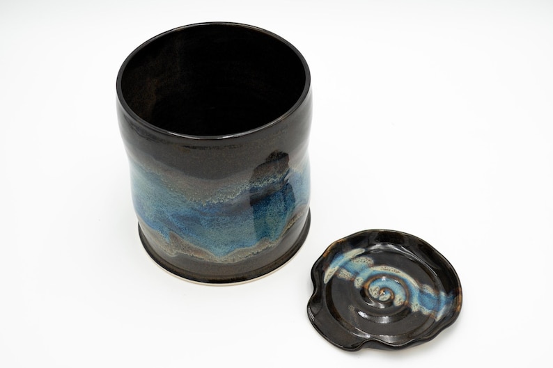 May include: A black ceramic jar with a blue and brown glaze. The jar has a lid with a swirl design.
