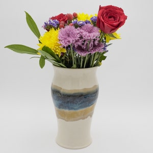 May include: A white ceramic vase with blue and brown stripes, filled with a bouquet of yellow, red, and purple flowers.