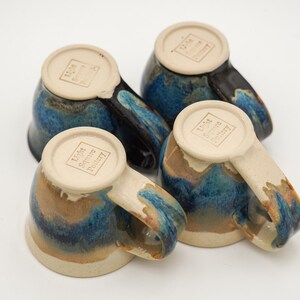May include: Four blue and brown ceramic mugs with a white glaze and the text "Lisa Scott Pottery" on the bottom.