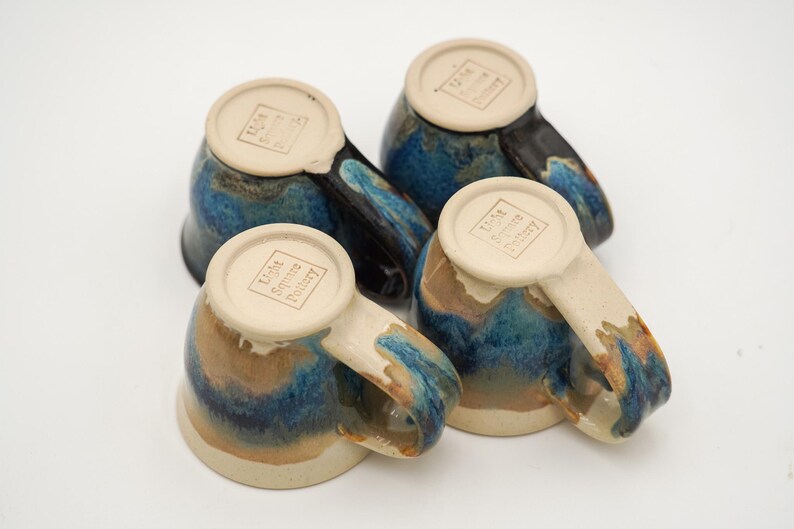May include: Four blue and brown ceramic mugs with a white glaze and the text "Lisa Scott Pottery" on the bottom.