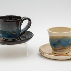May include: Two ceramic teacups and saucers with blue, brown, and white glaze. The cups have a rounded shape and a handle. The saucers are round and have a slight lip.