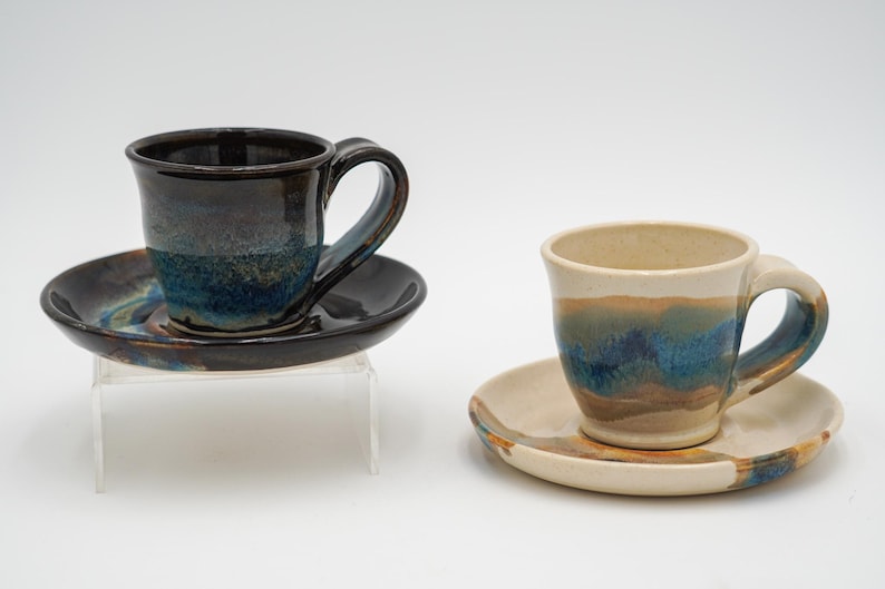 May include: Two ceramic teacups and saucers with blue, brown, and white glaze. The cups have a rounded shape and a handle. The saucers are round and have a slight lip.