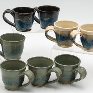 May include: Set of eight ceramic mugs with blue, green, and brown glaze. The mugs have a variety of shapes and sizes.