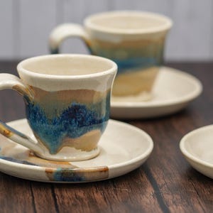 May include: Set of four ceramic coffee cups and saucers with a blue, brown, and white glaze. The cups have a rounded shape and a handle.