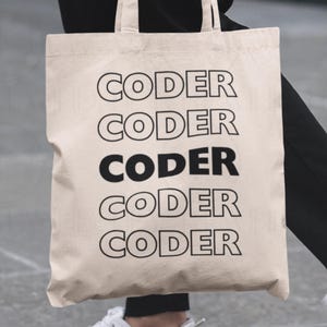 May include: A beige tote bag with the word "CODER" printed in black, repeated five times. The bag is held by a person wearing black pants and white sneakers. The bag's design is simple and modern.