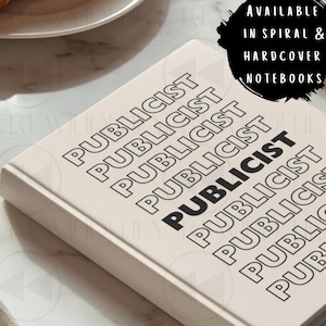 May include: A rectangular notebook with a cream-colored cover featuring the word PUBLICIST repeated in a diagonal pattern in black text. A black circular graphic on the cover contains the white text: AVAILABLE IN SPIRAL & HARDCOVER NOTEBOOKS.