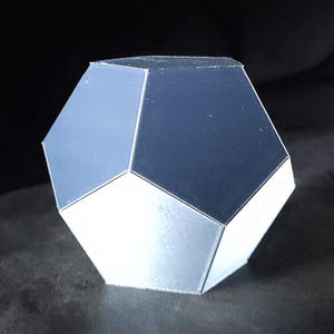 Peut inclure: Une forme géométrique argentée à 12 côtés. La forme est un dodécaèdre, une forme tridimensionnelle à 12 faces, 20 sommets et 30 arêtes.