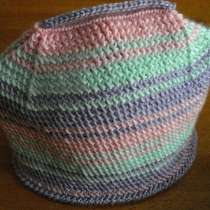 May include: A crocheted tea cozy in pink, green, and purple stripes. The cozy is made with a textured stitch and has a rounded shape.