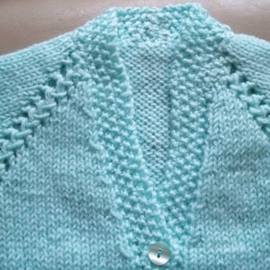 May include: A light blue knitted cardigan with a button closure and a detailed stitch pattern.