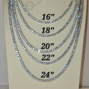 以下が含まれることがあります： 透明なキュービックジルコニアの石が付いた銀のテニスチェーンが5本。チェーンはマネキンに展示されており、長さが16インチ、18インチ、20インチ、22インチ、24インチと表示されています。
