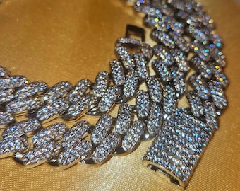 May include: A silver Cuban link chain necklace with a large, chunky design. The chain is covered in small, clear cubic zirconia stones that sparkle in the light.