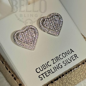 May include: A pair of sterling silver heart-shaped earrings with cubic zirconia stones. The earrings are in a white box with the words "BELLO BLING" and "CUBIC ZIRCONIA STERLING SILVER" printed on it.