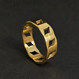Puede incluir: Un anillo dorado con un diseño de cortes en forma de diamante repetidos. El anillo está hecho de un metal brillante y reflectante y está sobre un fondo oscuro. El diseño del anillo es geométrico y moderno.