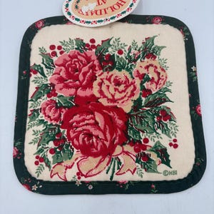 May include: A square fabric pot holder with a cream-colored center featuring a floral print of red and pink roses, green holly leaves, and red berries. The border is dark green with a small floral pattern. An oval tag reads HOLIDAY AT HOME.