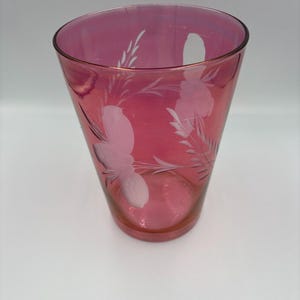 May include: A ruby-red glass with etched floral patterns. The glass has a flared shape and a smooth, polished finish. The etched designs are white and depict flowers and foliage. The glass is suitable for serving drinks.
