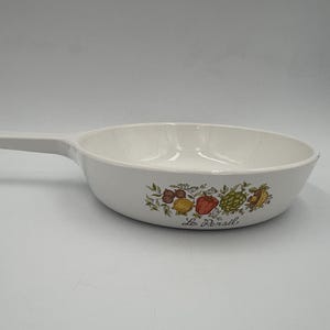 May include: White ceramic skillet with a handle. The skillet features a colorful floral and vegetable design with the text "Le Persil". The design includes illustrations of tomatoes, lemons, and other produce.