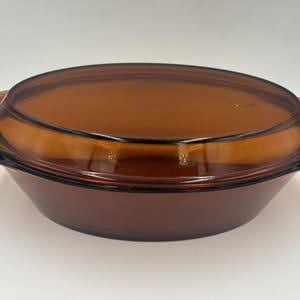 May include: Amber-colored glass casserole dish with a matching lid. The dish has a rounded shape with two handles on either side. The lid fits snugly on top, creating a complete and functional kitchenware item.