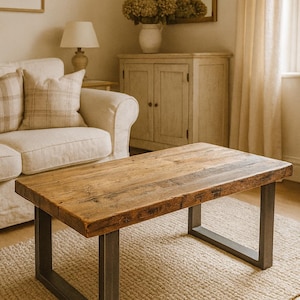 May include: A rectangular coffee table with a reclaimed wood top and dark grey metal legs. The table sits on a beige rug. The wood top has visible grain and knots. The table is approximately 120 cm long.