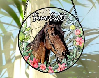 Pode incluir: Decoração de janela redonda em vitral com a cabeça de um cavalo castanho e a palavra "Snowball". O cavalo tem uma brida e é rodeado por flores cor-de-rosa e folhagem verde. Uma corrente preta está presa para pendurar.