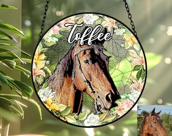 Pode incluir: Retrato redondo de cavalo em estilo vitral com o nome "Toffee" em escrita cursiva. O cavalo castanho usa uma sela, rodeado por uma grinalda floral de flores brancas, rosas e amarelas. Uma corrente preta pende do topo.