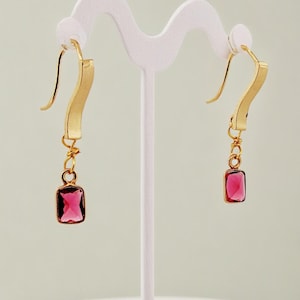 May include: A pair of gold earrings with a pink square gemstone dangling from each earring.