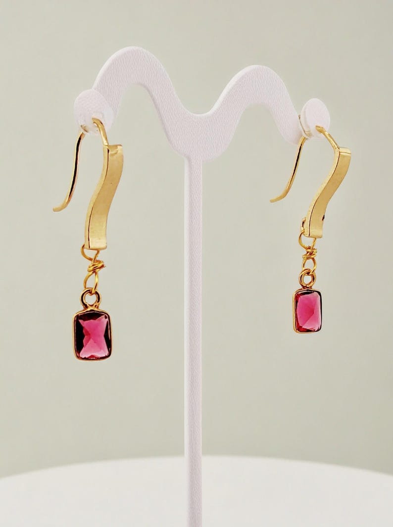 May include: A pair of gold earrings with a pink square gemstone dangling from each earring.