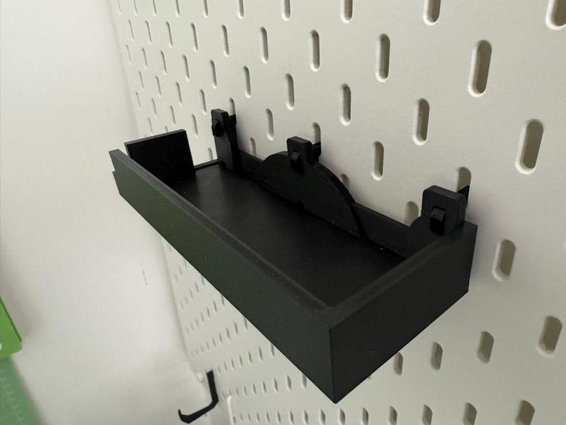 May include: Black shelf with a black metal bracket mounted on a white pegboard wall.
