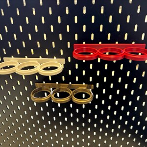 May include: Three different colored metal pegboard organizers for holding items like tools or other small objects. The organizers are mounted on a black pegboard.