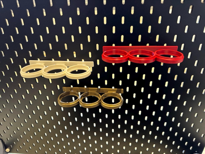 May include: Three different colored metal pegboard organizers for holding items like tools or other small objects. The organizers are mounted on a black pegboard.