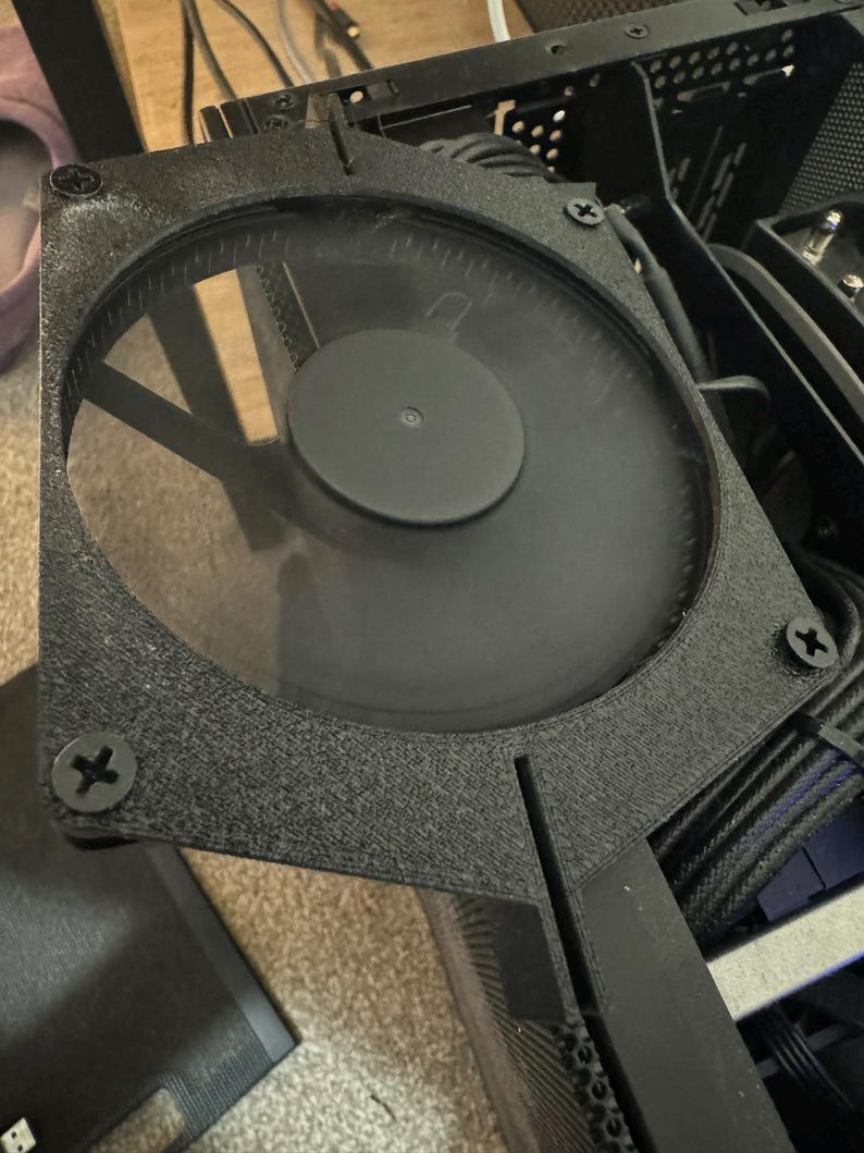 以下が含まれることがあります： 透明なプラスチックカバーと黒い金属フレームが付いた黒いコンピューターファン。ファンはコンピューターケースに取り付けられています。