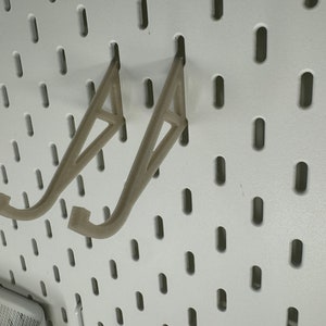 May include: Two beige plastic wall mounted hooks for hanging items on a pegboard.