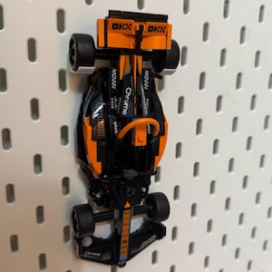 Op de afbeelding: Een zwarte en oranje Lego raceauto met de woorden "Chrome" en "spin" aan de zijkant. De auto hangt aan een prikbord.