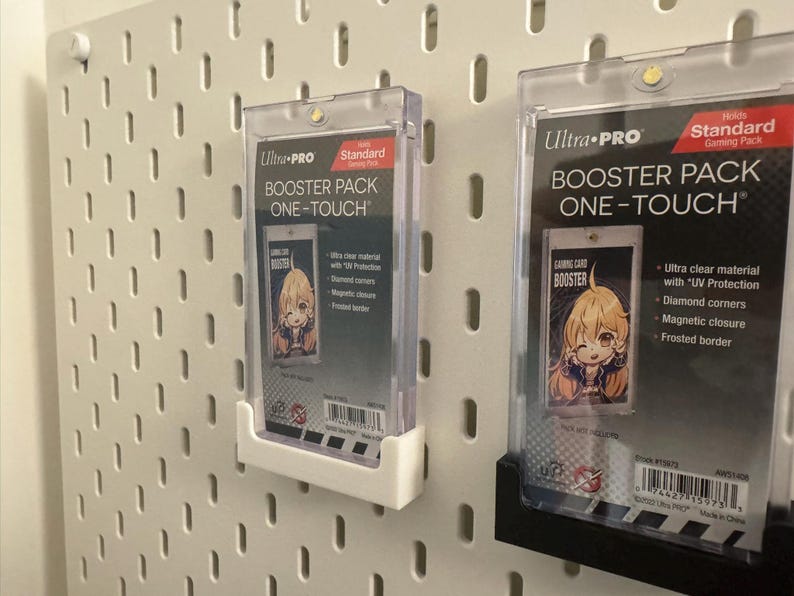 以下が含まれることがあります： 2つの透明なUltra-Pro Booster Pack One-Touchケース。それぞれに漫画のキャラクターが描かれたゲームカードが入っています。ケースは白いペグボードに取り付けられています。ケースはUV保護、ダイヤモンドコーナー、マグネット開閉、フロストボーダーを備えています。